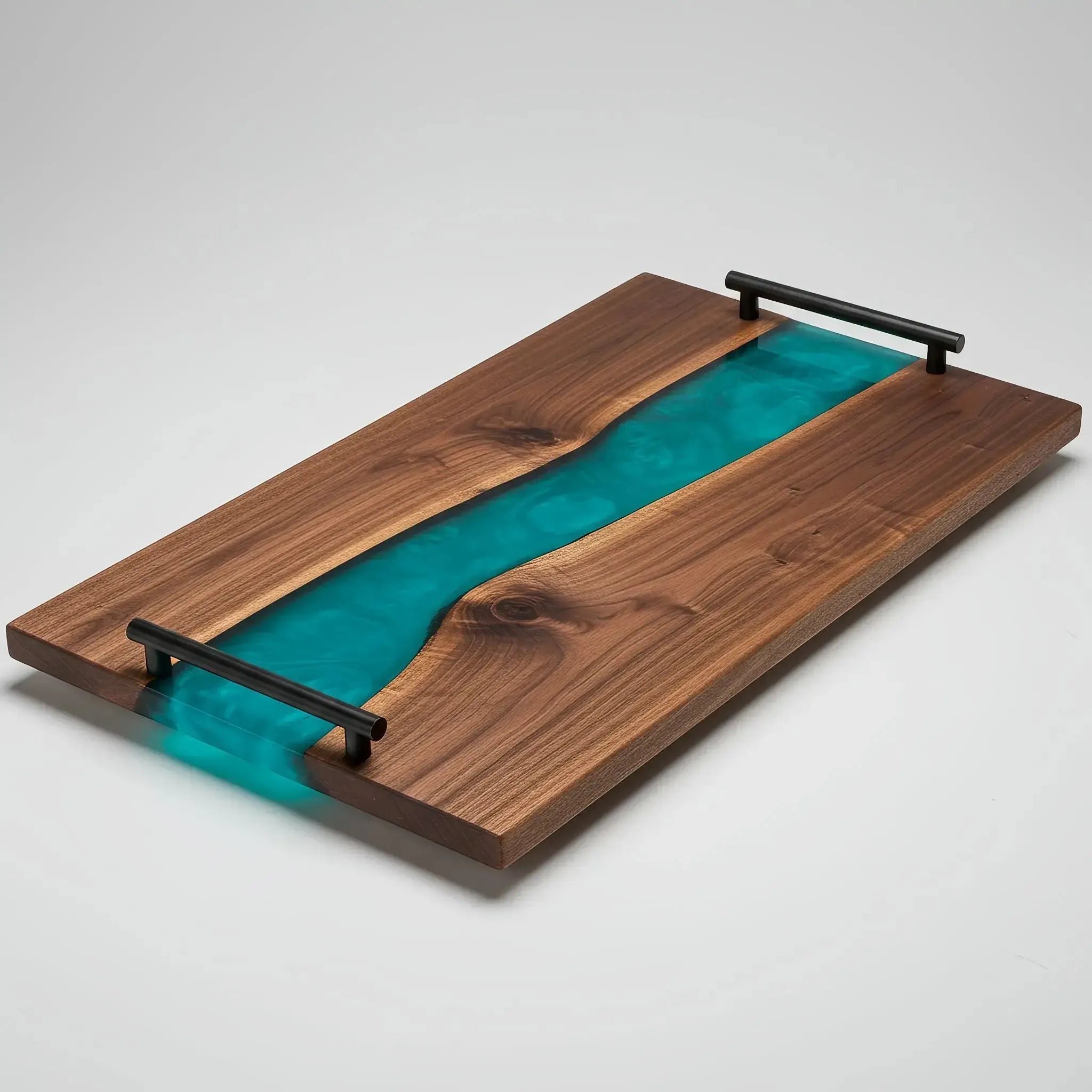 charcuterie board, 18 inches by 9 inches, made from live edge black walnut wood with a deep, glossy teal blue epoxy river flowing through the center. The resin has a rich, ocean-inspired tone—somewhere between deep teal and sapphire—with soft swirling patterns and a slightly muted, elegant finish. The board has a smooth, polished surface with warm walnut grain and visible natural figuring. Matte black metal handles are attached at each end.