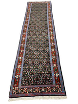 Long narrow runner rug with dense floral motifs in black, cream, and red, framed by a red border with geometric floral patterns and blue trim edges.