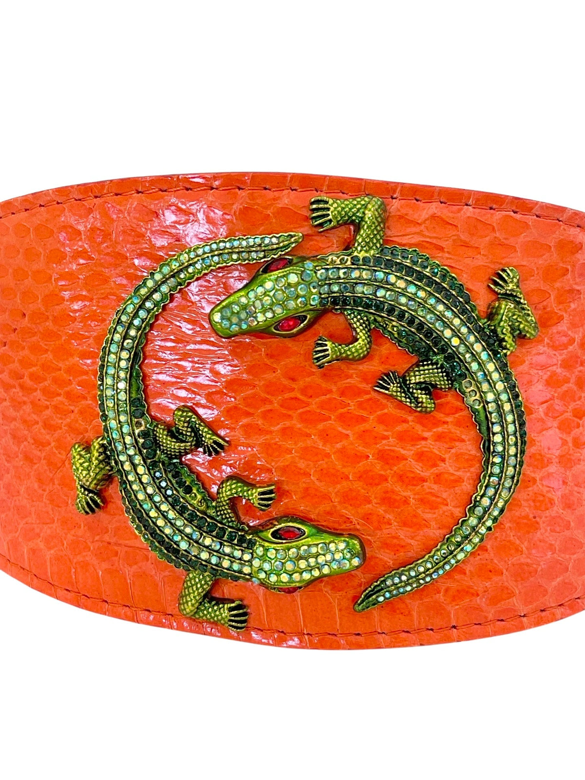 Two green rhinestone-studded alligator embellishments arranged in a circular pattern on a textured orange snake-patterned surface.