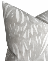 Close-up of a grey pillow cover featuring an abstract white pattern resembling elongated leaf shapes on a textured fabric surface.