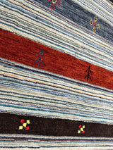 Close-up of a hand-knotted Indo-Gabbeh rug featuring horizontal stripes in blue, red, and black with small geometric and tree-like motifs embroidered.