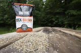 Bag of Big Tine Buck Brunch food plot mix standing on a weathered wooden surface with scattered seeds in front, set against an outdoor forest background.