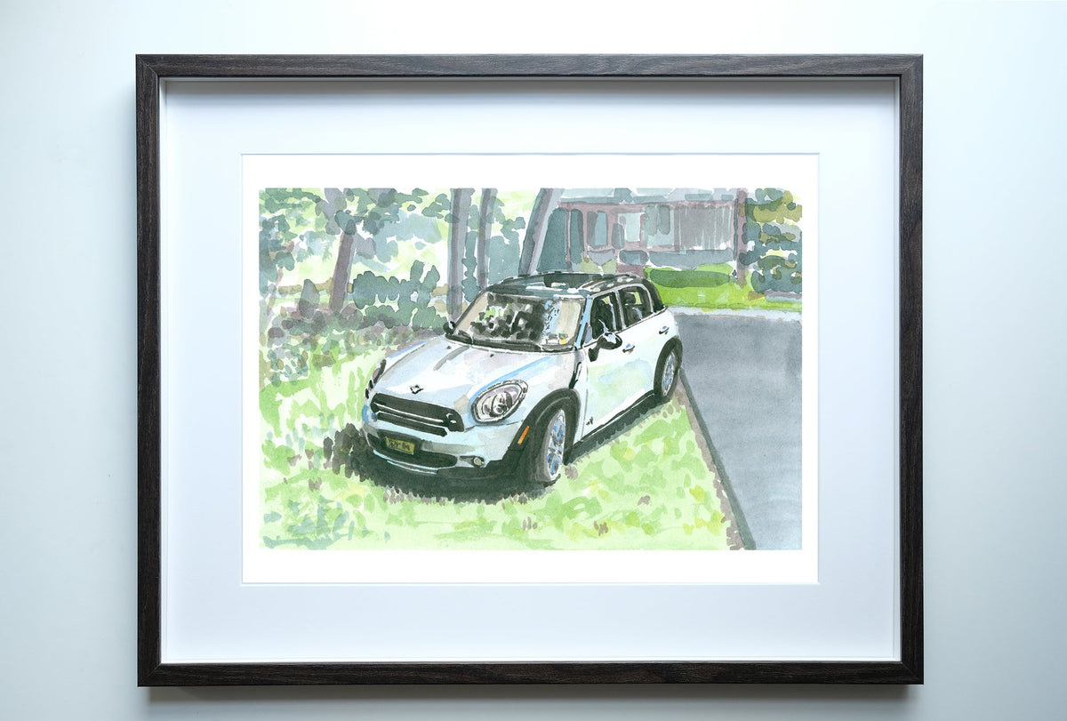 Framed watercolor painting of a white Mini Cooper Countryman parked on a grassy lawn beside a driveway with trees and a house in the background.