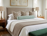 Neutral-toned bed with taupe Freedia pillow covers featuring circular patterns, a light green bolster pillow, and matching taupe throw blanket in a softly lit bedroom.