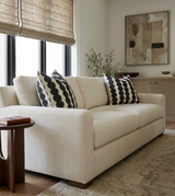 Beige sofa with two black and white circular patterned pillows, near a wooden side table and framed abstract art on a light wall.
