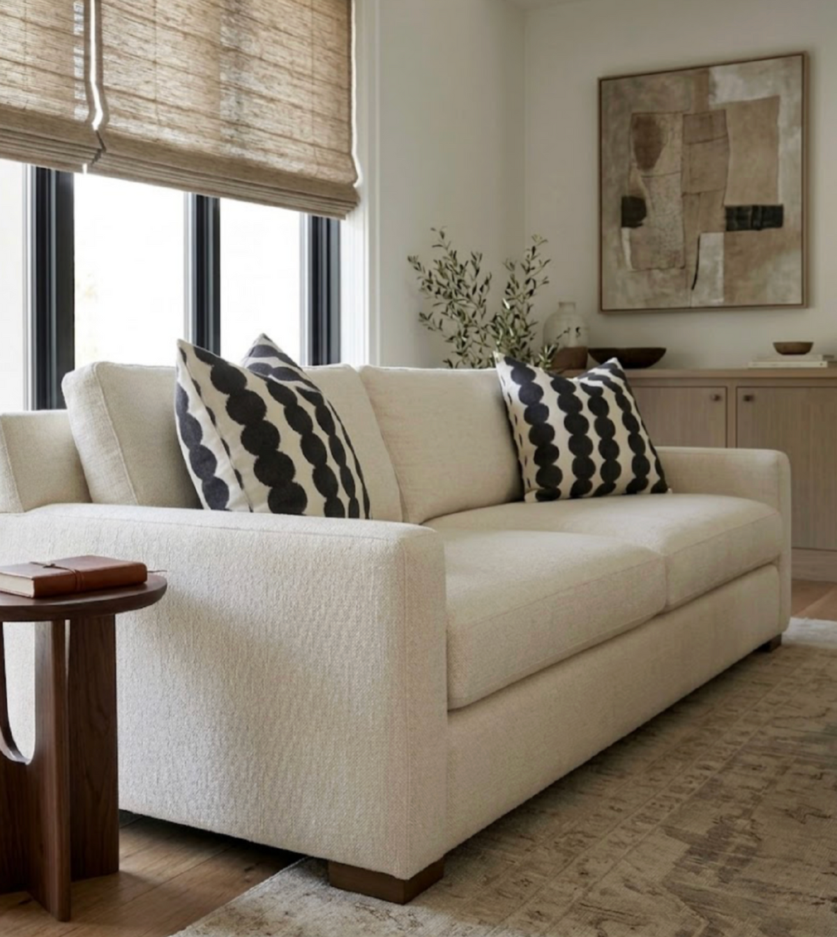 Beige sofa with two black and white circular patterned pillows, near a wooden side table and framed abstract art on a light wall.