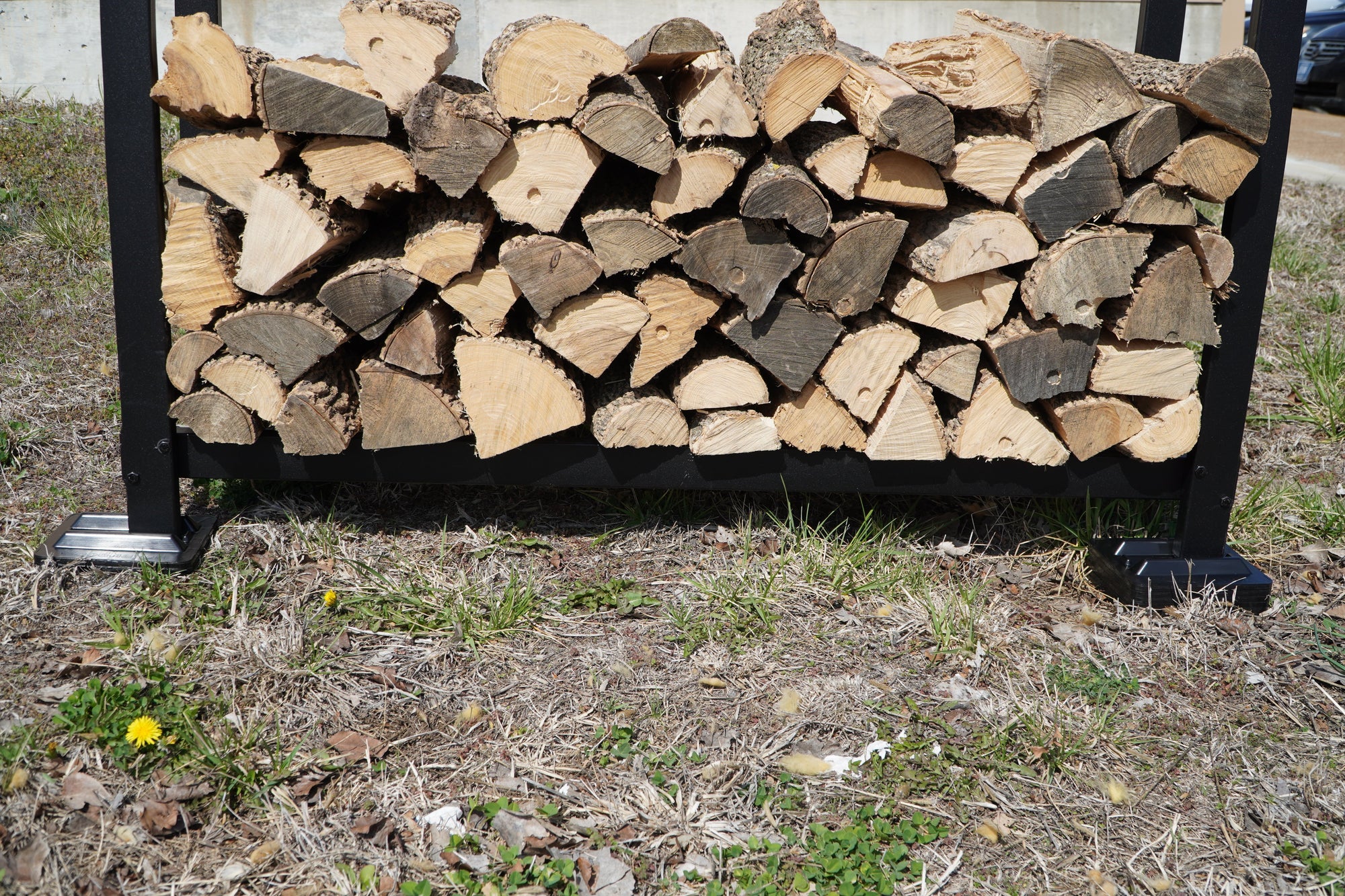 Black and brown firewood rack support bases stacked on concrete and grass surfaces