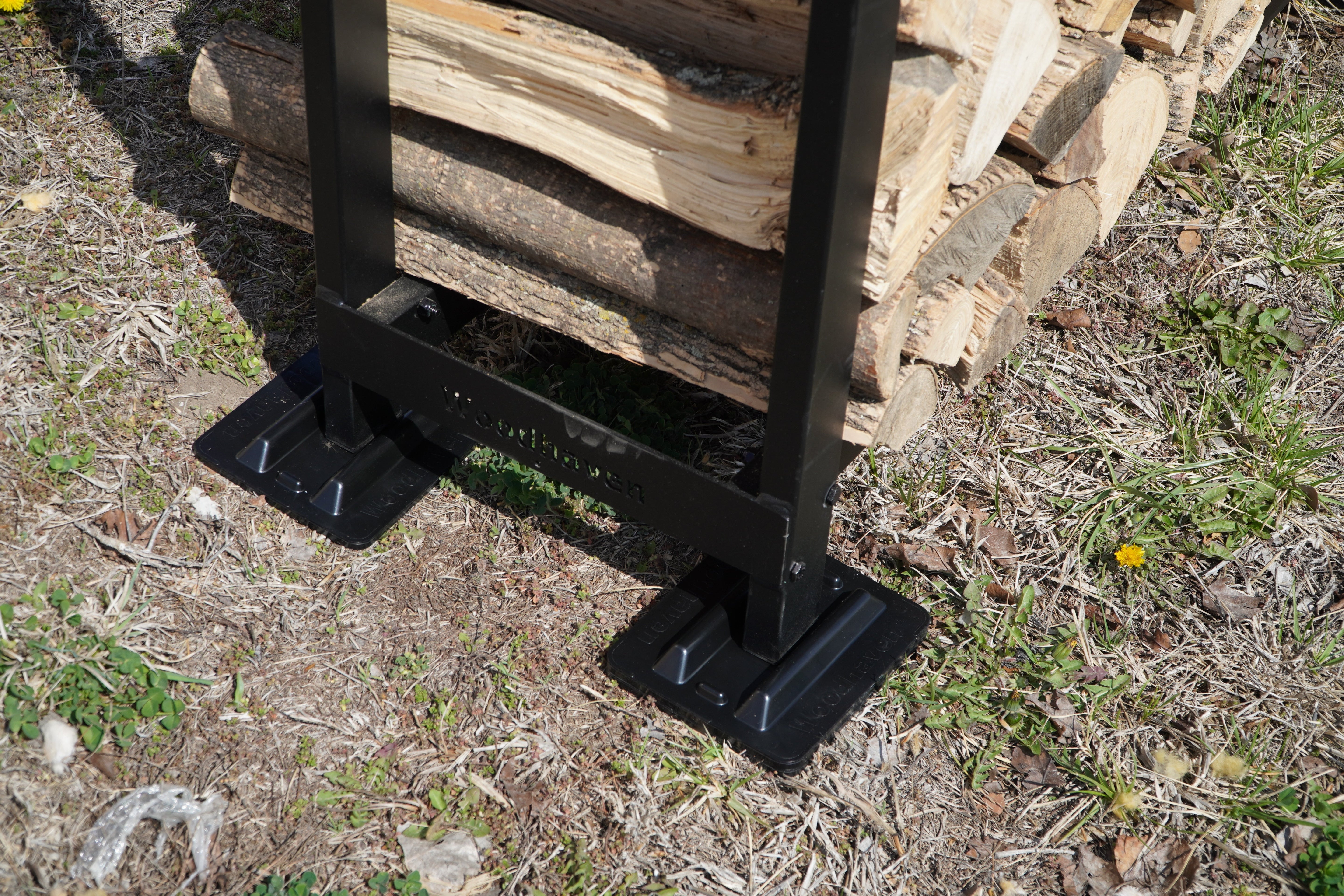 Black and brown firewood rack support bases stacked on concrete and grass surfaces