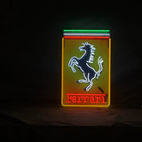 Neon sign featuring a prancing white horse outlined in blue on a yellow rectangle with red neon 'Ferrari' text below and green, white, and red stripes above it against a black background.