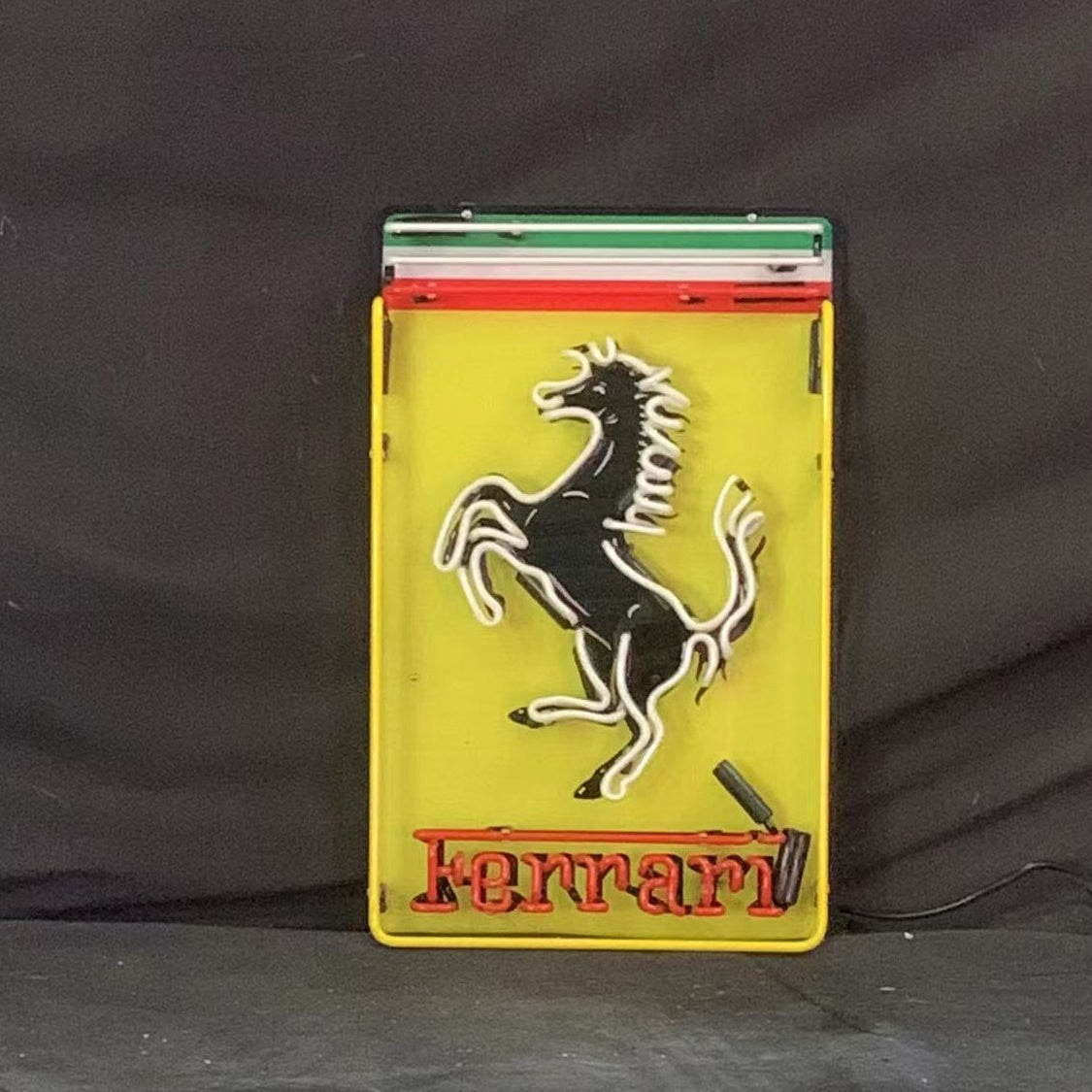 Rectangular neon sign with a yellow background featuring a black prancing horse outlined in white, topped by green, white, and red horizontal bands, and 'Ferrari' in red neon at the bottom