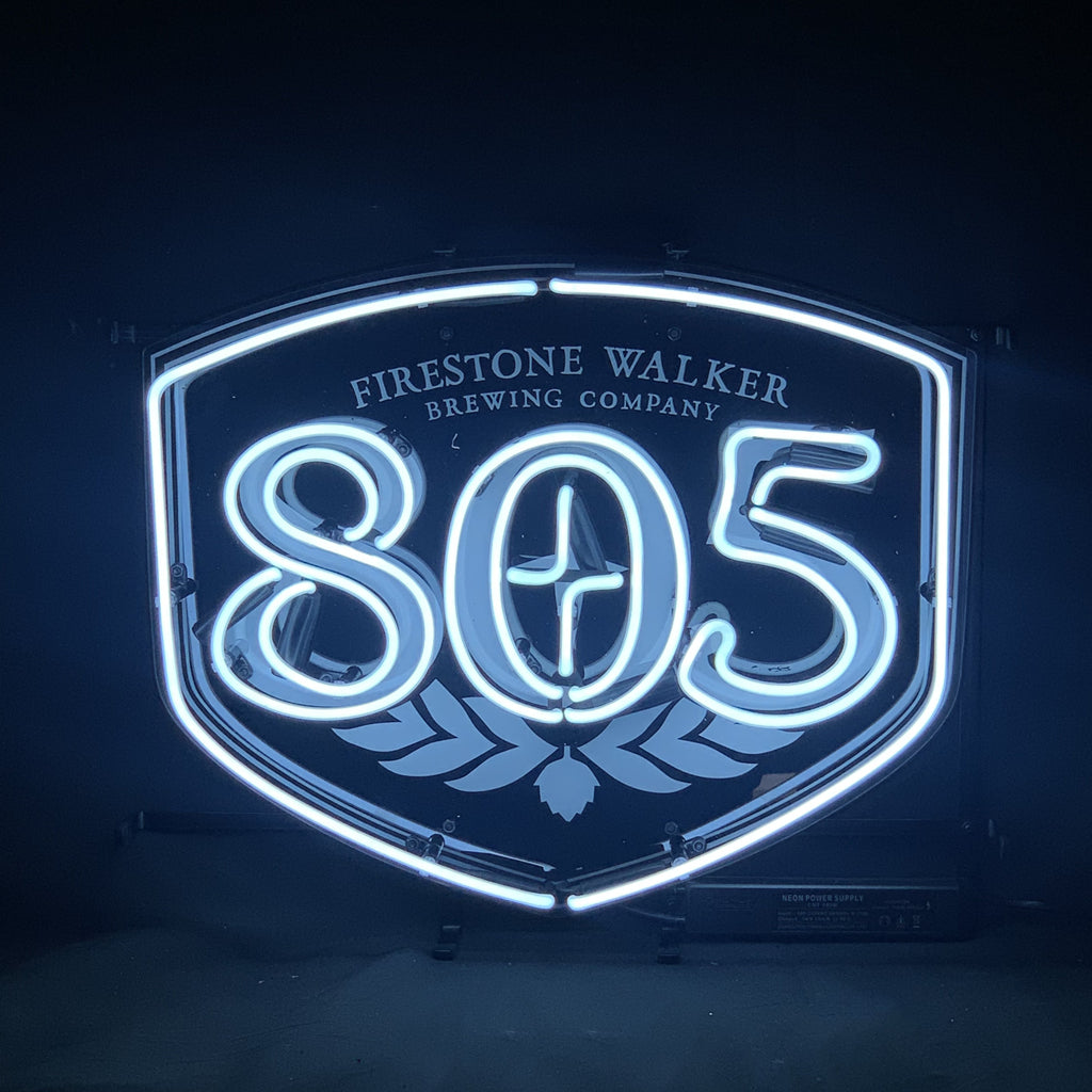 White neon sign shaped like a shield with 'Firestone Walker Brewing Company' text above and large '805' numbers centered, glowing against a dark background.