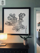 Black and white tree ring print resembling coral or a branch, framed and hung on a light gray wall above a dark wooden console with a lamp and potted orchid.