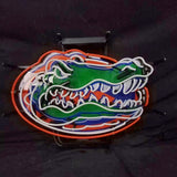 Neon sign shaped like a green alligator head with white teeth, orange and blue accents on a black background