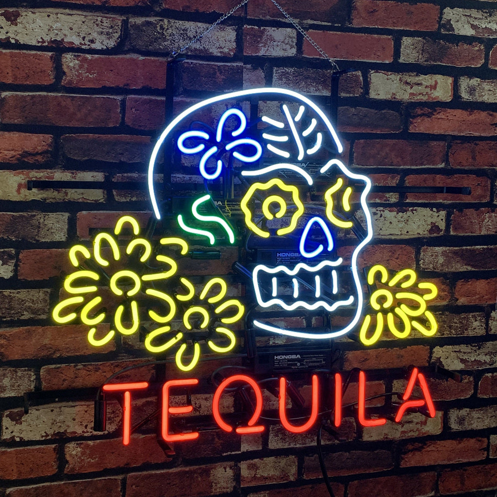 Neon sign of a white and blue skull decorated with yellow flowers and green lines above the red word 'TEQUILA' on a brown brick wall