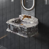 Wall-mounted marble sink with fluted vertical grooved sides in white with dark veining, paired with gold faucet and mounted below an oval backlit mirror on black wall panels.