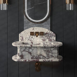 Wall-mounted fluted marble sink with deep purple and white veins, featuring bronze faucet and illuminated oval mirror above on dark vertical paneled wall.