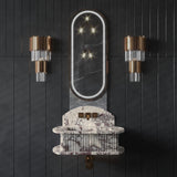 Wall-mounted fluted marble sink with grey, white, and burgundy veining, beneath an oval mirror with integrated LED light, flanked by two brass and glass sconces on dark panel walls.