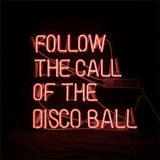 Rectangular pink neon light sign displaying the phrase 'FOLLOW THE CALL OF THE DISCO BALL' in uppercase letters against a black background.