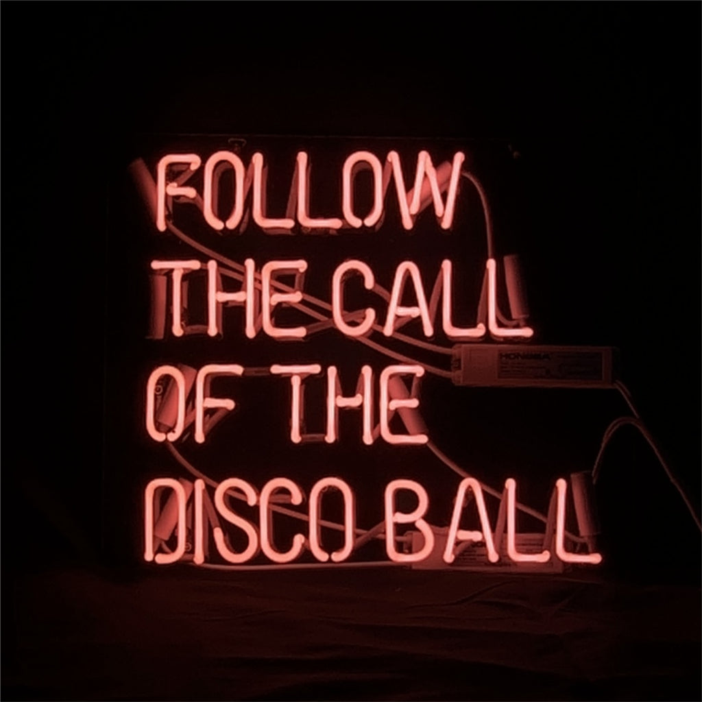 Rectangular pink neon light sign displaying the phrase 'FOLLOW THE CALL OF THE DISCO BALL' in uppercase letters against a black background.