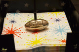 Handcrafted silver napkin holder shaped like an American football, resting on colorful starburst patterned napkins inside a black container with star cutouts.