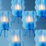 Seven blue lamps with wavy translucent shades glowing warmly, each supported by three short blue legs, arranged against a matching blue background.