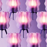 Group of translucent wavy-shaped lamps with purple and pink hues, each standing on three dark legs against a purple background.