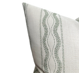 Close-up of beige outdoor pillow cover with vertical moss green wavy and dotted stripes, showing fabric texture and clean stitching at the corner.