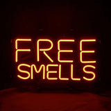 Bright orange neon sign with all-capital letters spelling 'FREE SMELLS' on a black background, glowing evenly with a slight reflection below.