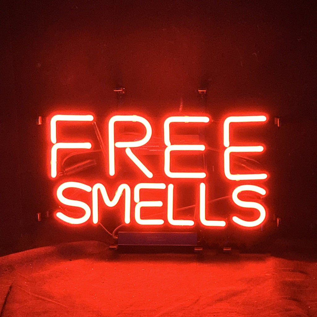 Free Smells Neon Sign featuring glowing text in neon glass tubes on a metal grid backing, lit indoors