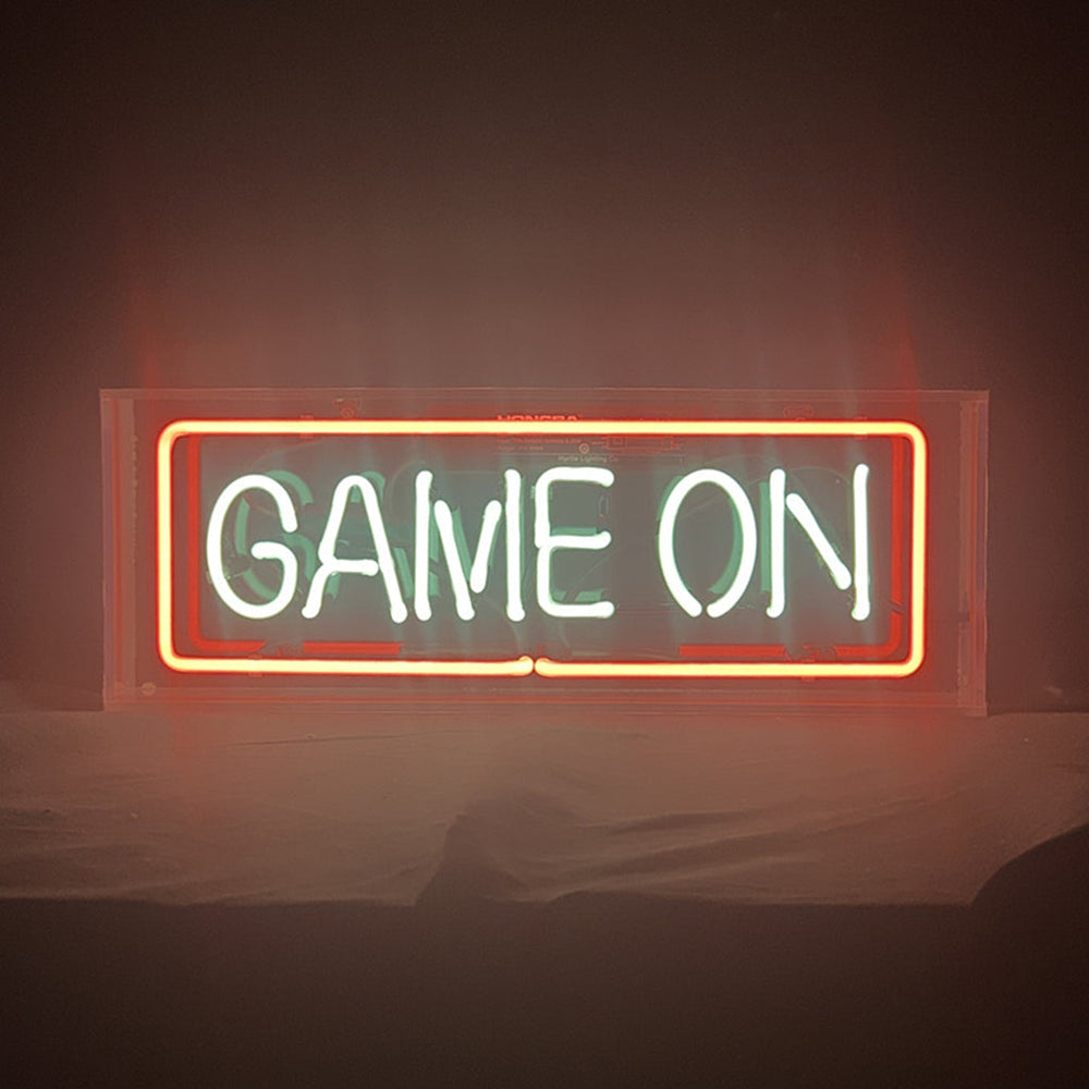 Game On Neon Sign illuminated with bright white light on acrylic backing hanging on a textured wall