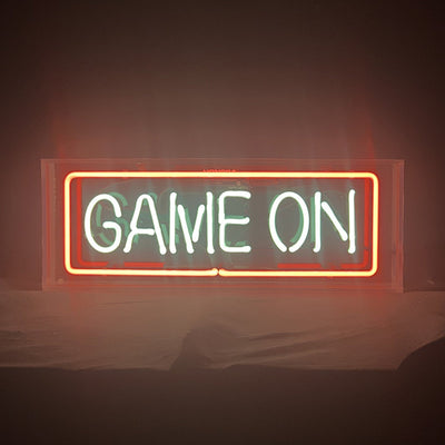 Game On Neon Sign illuminated with bright white light on acrylic backing hanging on a textured wall