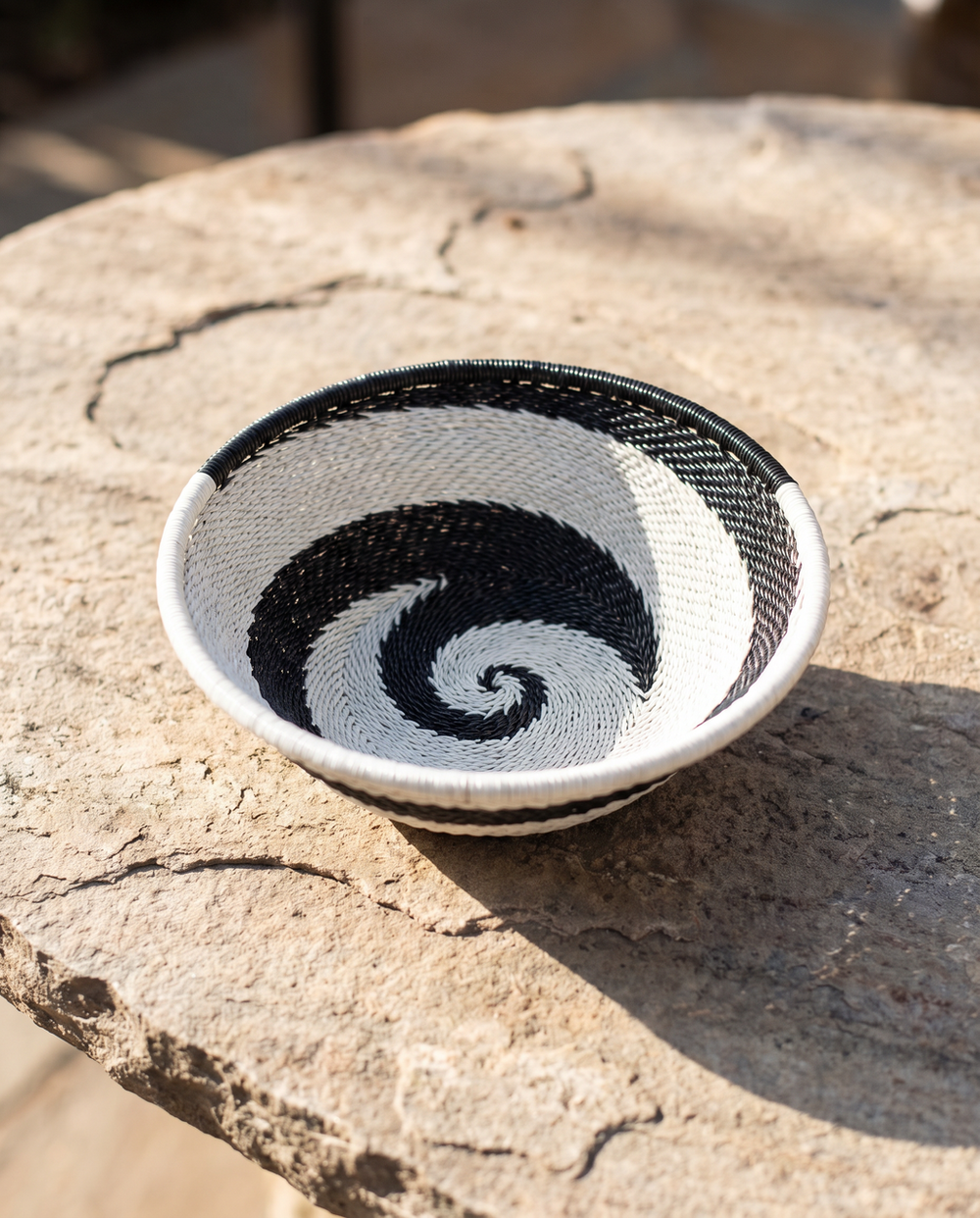 Small black and white wire basket with a spiral pattern, shown on a textured stone surface in natural light