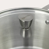 Close-up of a clear glass lid with a stainless steel knob engraved with CRISTEL, showing brushed metal surface and part of the pot handle on a white background.