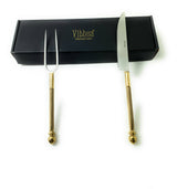 Set of two stainless steel carving tools with gold-toned textured handles, including a fork with two prongs and a knife with a straight-edged blade, displayed alongside a black box.