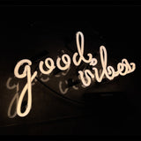 White neon sign spelling 'good vibes' in cursive on a dark background casting subtle shadows.