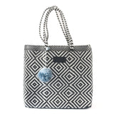 Black and white geometric patterned woven tote bag with double handles and a single light blue pom-pom accessory hanging on the front.