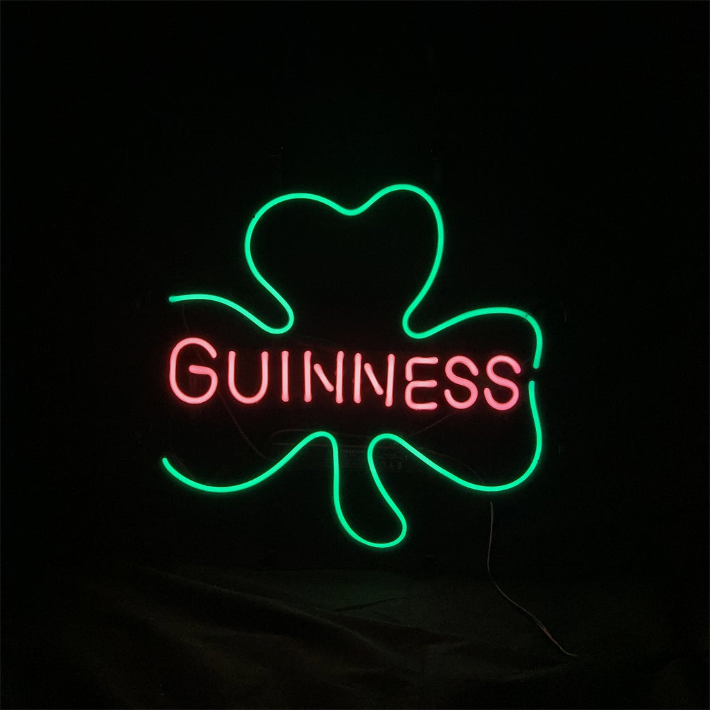 Green neon outline of a three-leaf clover surrounding the pink neon word 'GUINNESS' on a black background.