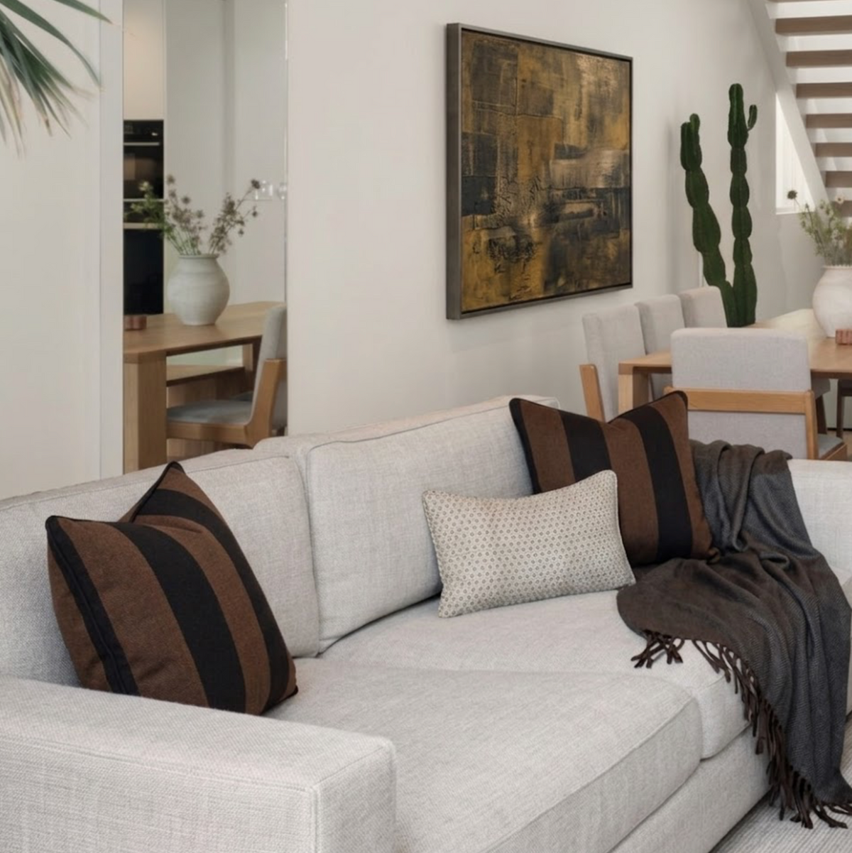Light gray sofa with two large brown and black striped pillows and a smaller beige patterned pillow, accompanied by a dark brown throw blanket on the right side.