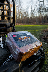 Rectangular Big Tine Nitro Mineral Brick with dark reddish-brown color and black label placed outdoors on a black surface with grass and trees in the background.