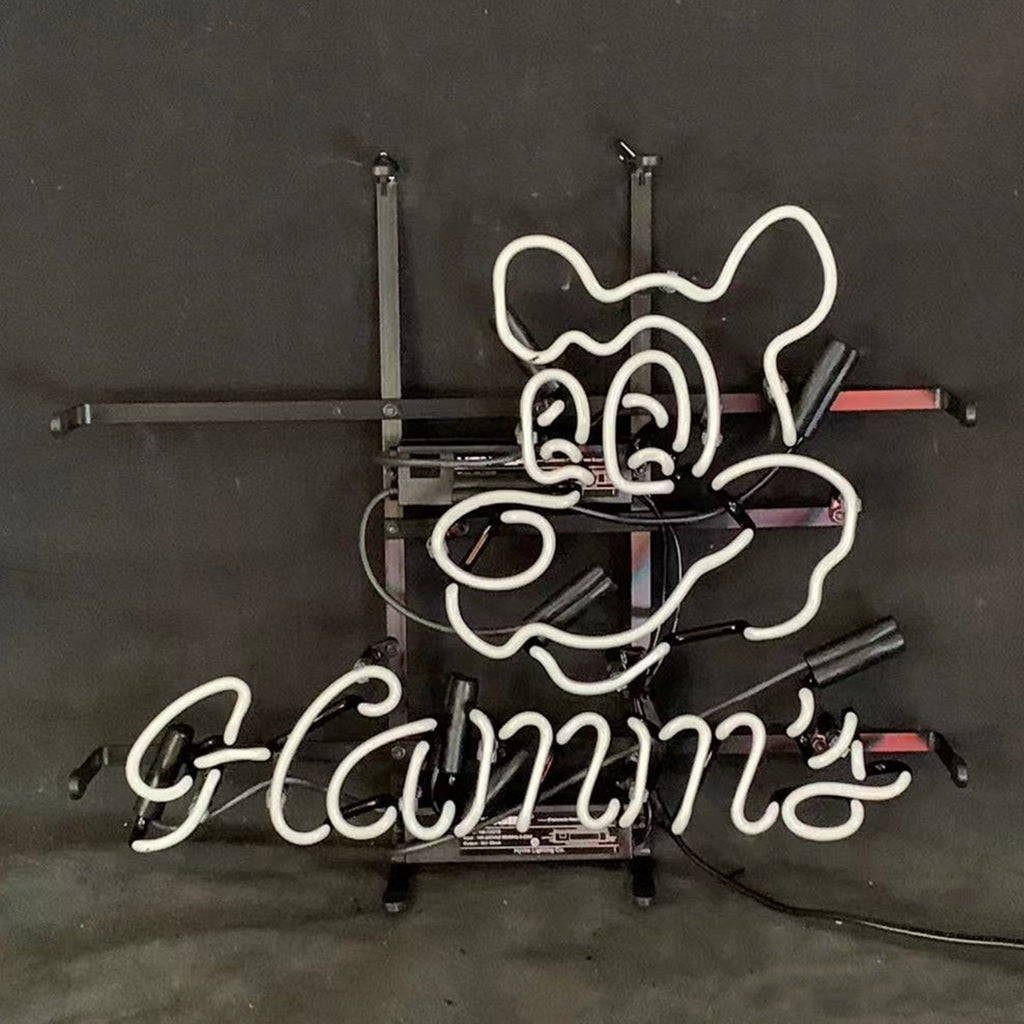 White neon sign shaped like a cartoon bear's face above cursive text reading "Hamm's" on a dark background with visible black mounting frame.