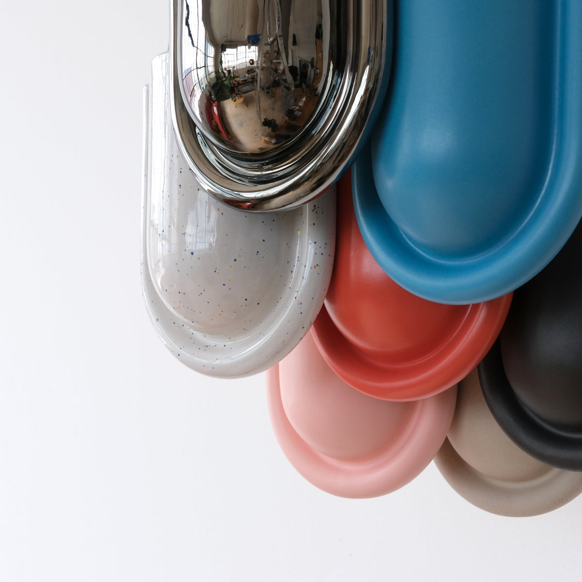 Stack of oval-shaped planters in metallic, speckled white, blue, red, pink, black, and beige colors arranged vertically against a white background.
