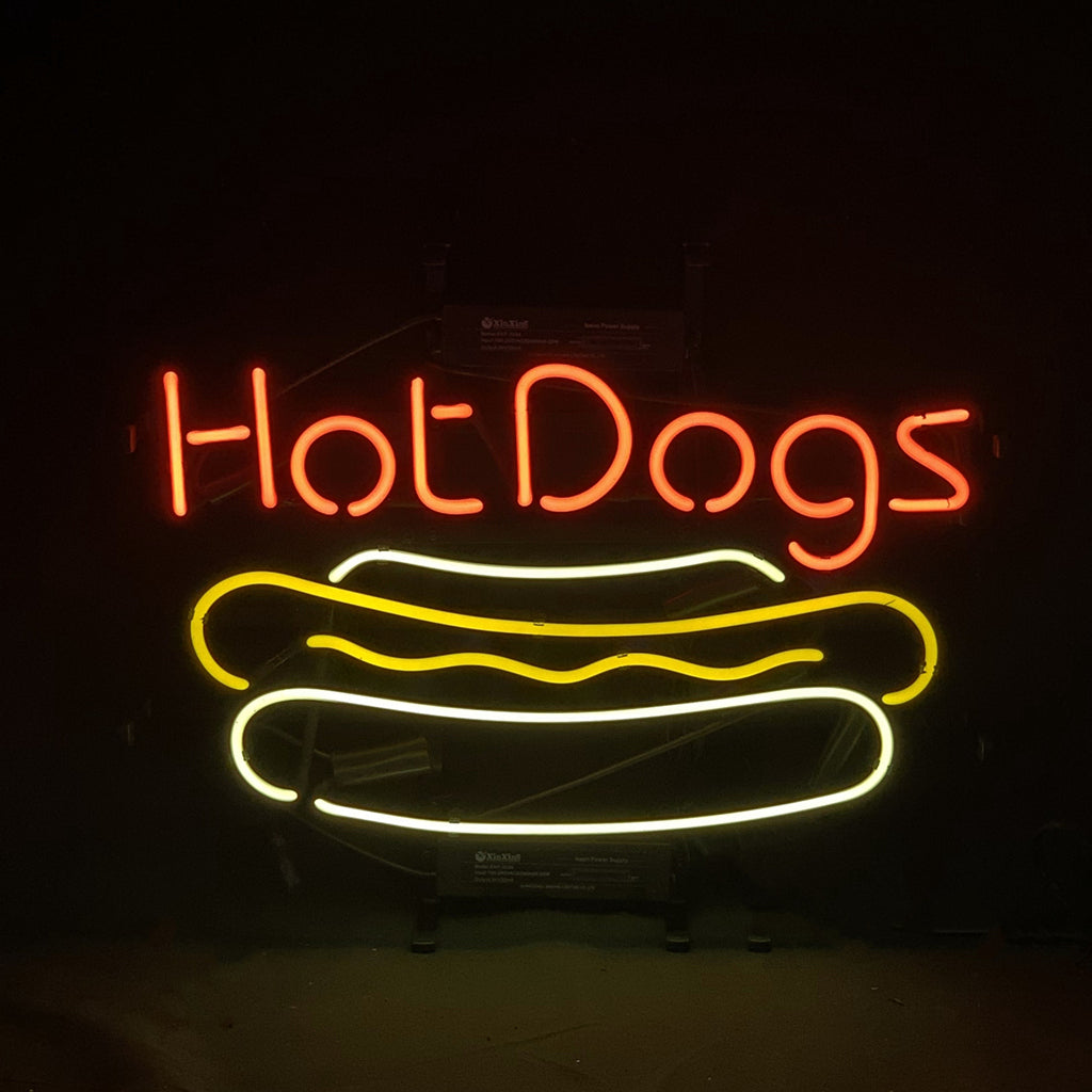 Neon sign displaying the words 'Hot Dogs' in red above a stylized yellow and white hot dog graphic on a black background.
