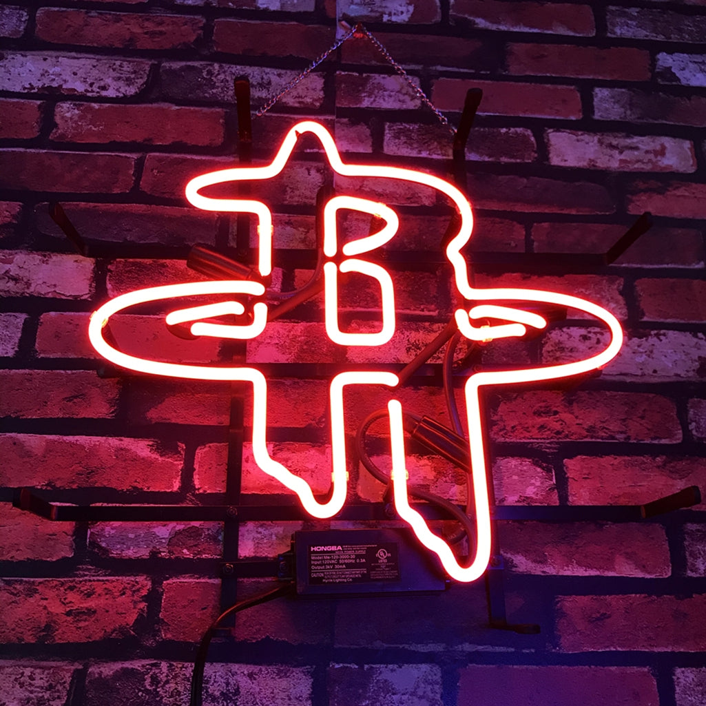 Bright red neon sign in the shape of the Houston Rockets logo mounted on a dark red and purple brick wall.