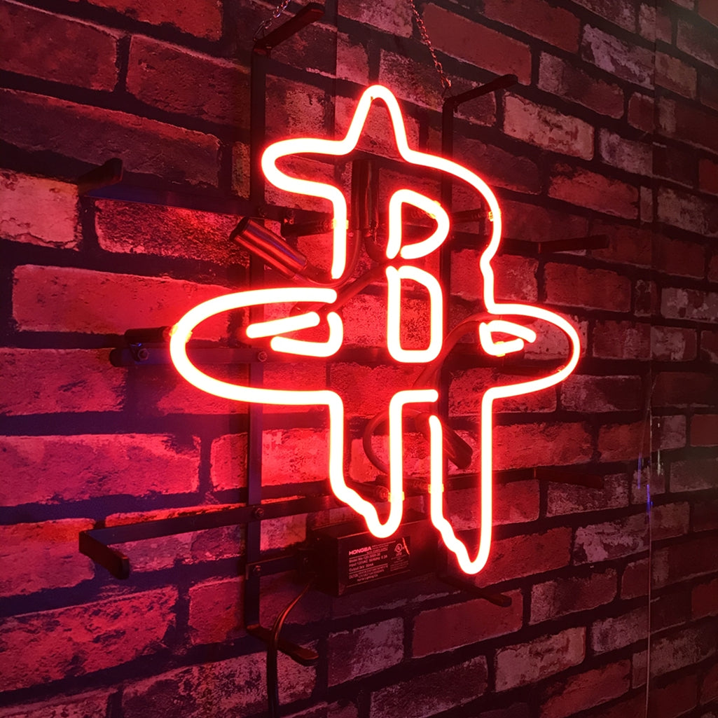 Red neon sign shaped like the intertwined letters R and H mounted on a dark red brick wall, casting a warm glow on the bricks.