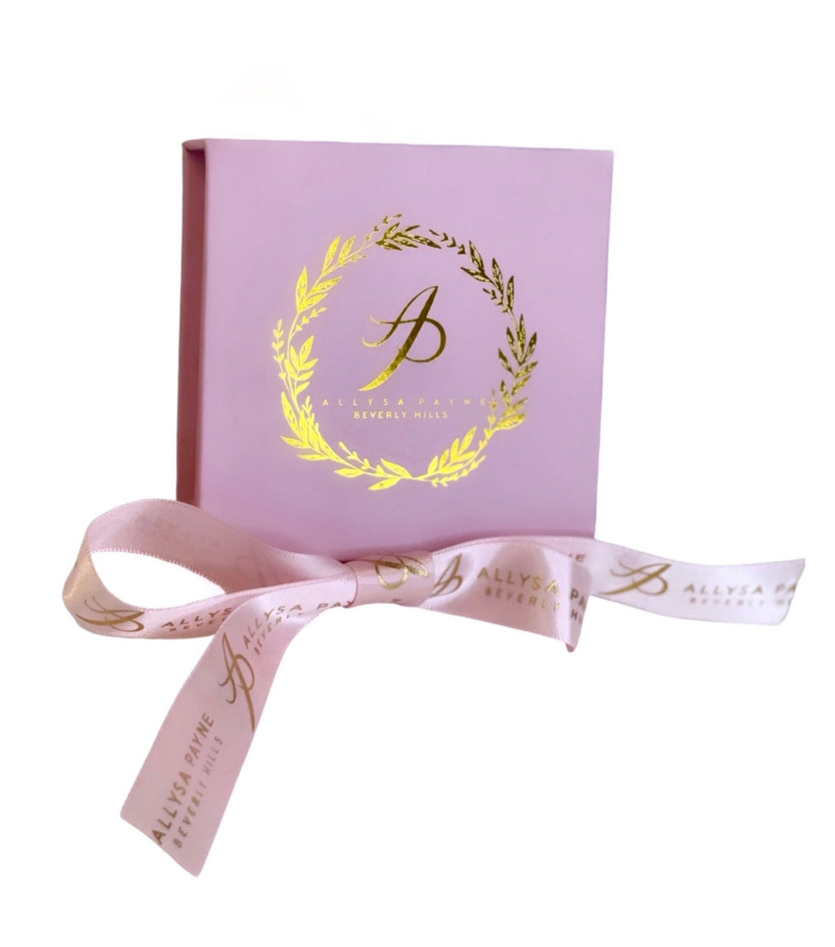 Light pink square box with a gold laurel wreath and stylized 'AP' logo, accompanied by a matching pink ribbon printed with 'Allysa Payne Beverly Hills' in gold.