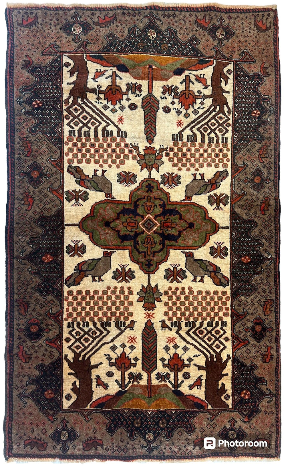 Antique Baloch rug with ivory central field featuring symmetrical geometric and floral motifs in brown, green, and rust, framed by a dark border with intricate patterns.
