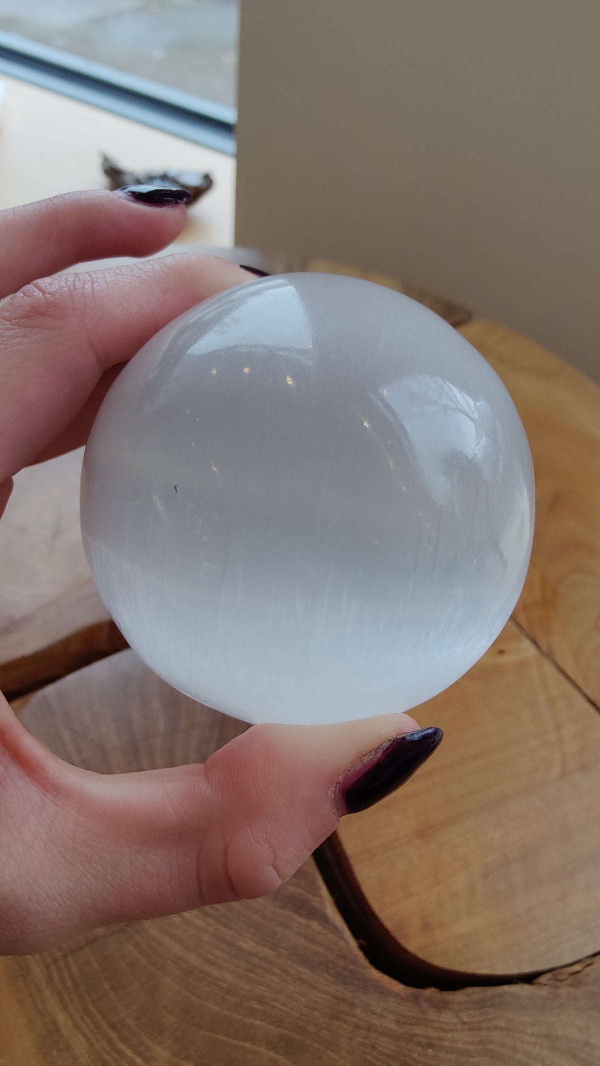 Hand holding a smooth, translucent white sphere with subtle striations, resting above a round wooden surface with natural grain patterns.