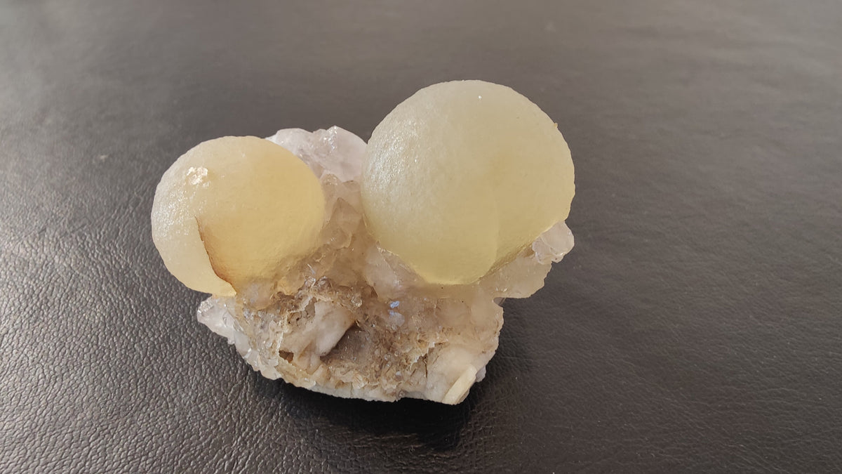 Two pale yellow fluorite spheres resting on an irregular white and light gray quartz matrix with a rough texture, shown against a dark background.