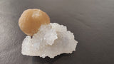 Tan spherical fluorite ball resting on an irregular cluster of translucent white quartz crystals against a dark background.