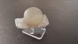 Translucent pale green fluorite sphere resting on a cluster of white quartz crystals, displayed on a clear acrylic stand against a brown background.
